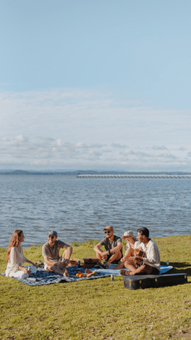 A group of friends having a picnic along the water with a jetty in the background